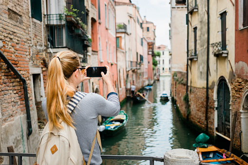 Young woman taking a photo on her smartphone of a canal in Venice, Italy