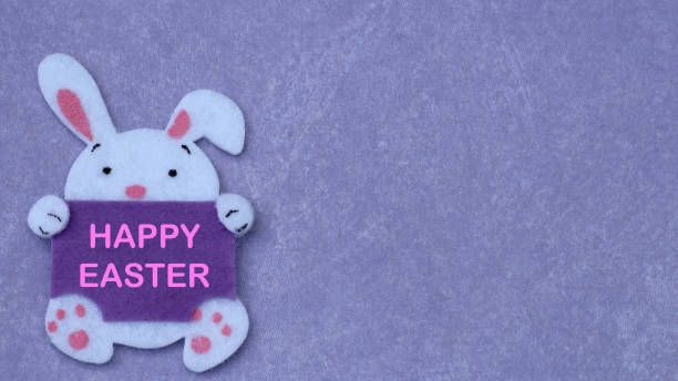 felt craft easter bunny holding a blank sign on a purple background with writing space