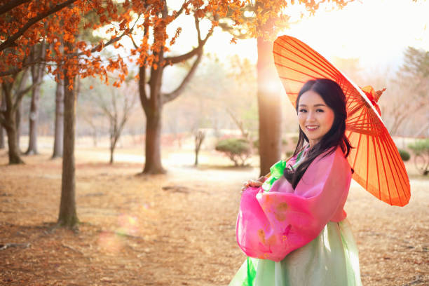 una chica coreana con un hanbok sosteniendo un paraguas rojo. hermosa hembra que lleva hanbok tradicional coreano con hojas de arce en hojas de otoño, corea. mujeres turistas asiáticas. - south corea fotografías e imágenes de stock