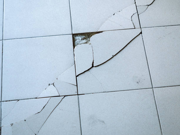 istock Close-up photo of light gray tile with large diagonal cracks and chips. 1206304204