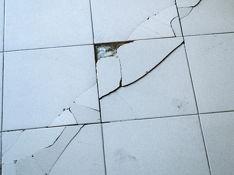 Close-up view of light gray tile with large diagonal cracks and chips.