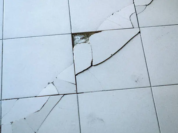 Photo of Close-up photo of light gray tile with large diagonal cracks and chips.