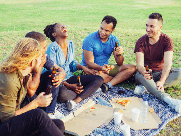 istock Happy smiling people drinking beer and eating pizza during picnic. 1206314751