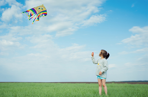 Little girl playing with a kite on a green field