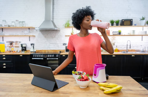 African American woman at home drinking a smoothie Portrait of a happy African American woman at home drinking a smoothie in the kitchen yogurt photos stock pictures, royalty-free photos & images