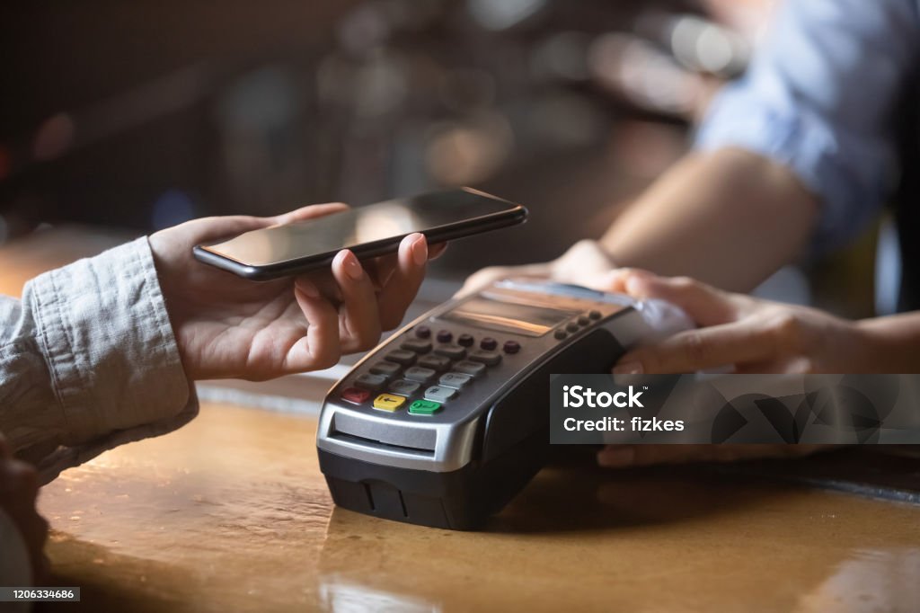 Client paying on terminal using smartphone nfc method Close up of female client hold smartphone paying for order using modern easy nfc technology, waiter give card reader machine for customer make payment transaction with cashless contactless method Paying Stock Photo