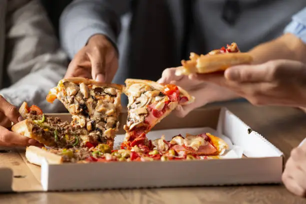 Photo of Close up of multiethnic friends share delicious pizza