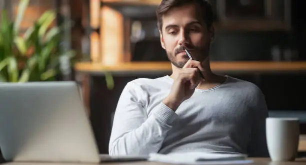 Photo of Pensive male thinking over problem solution working on laptop
