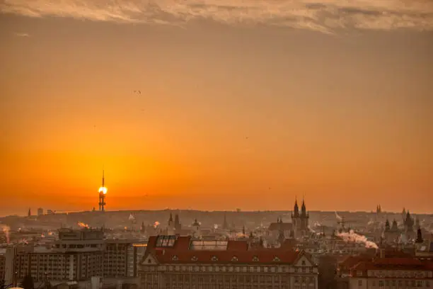 Photo of prague tv tower at sunrise wirh roofs and birds flying