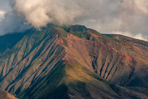Lahaina, Maui, Hawaii, USA. - January 12 2012: Closeup of green-brown mountain, part of Haleakala volcano range under thick gray-white cloudscape.