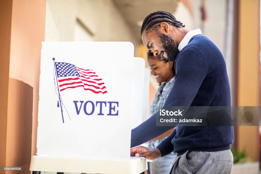 Millenial Black Man and Woman Voting in Election A millennial black man and woman voting at a voting booth in an election. Voting Stock Photo
