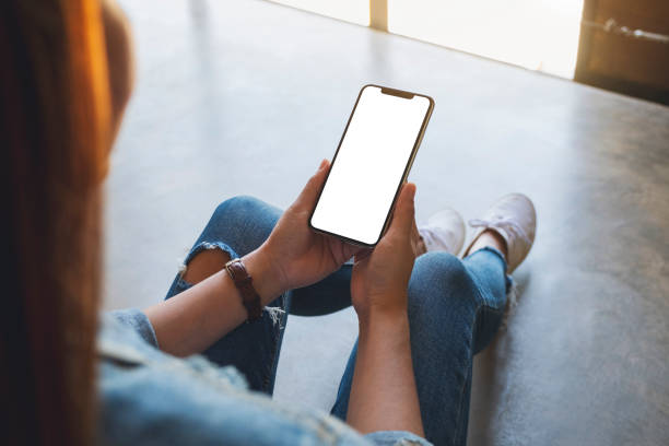 istock a woman holding black mobile phone with blank white screen while sitting on the floor 1206363837