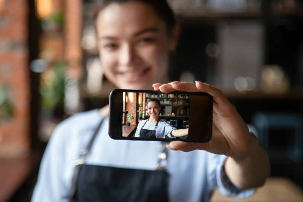istock Smiling waitress hold cellphone making selfie in restaurant 1206372129