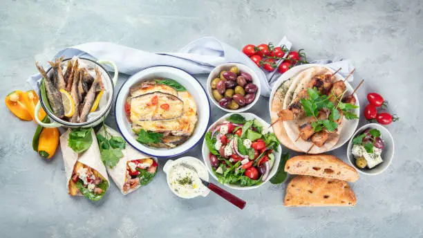 Greek food on grey background. Moussaka, gyros,souvlaki, pita, salad, olives and vegetables. Traditional different types of greek dishes. Top view, flat lay