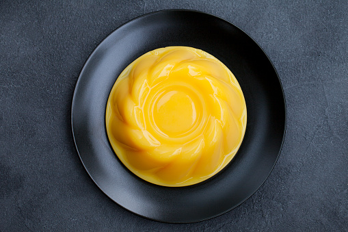 Mango pudding, jelly, dessert on black plate. Grey stone background. Top view.