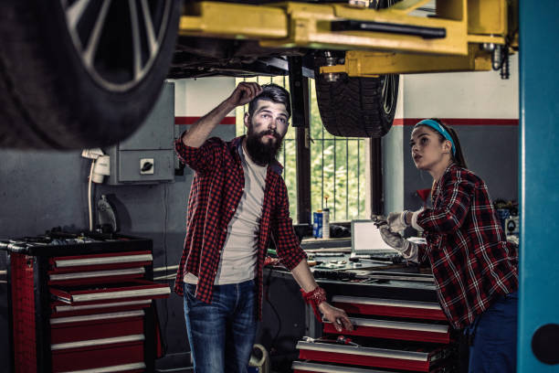 dos jóvenes colegas mecánicos de automóviles que dan servicio al coche - adult manual worker automobile industry transportation fotografías e imágenes de stock