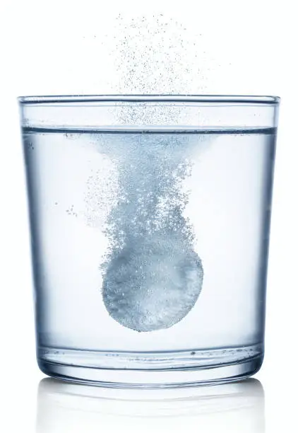 Photo of Effervescent tablet dissolving in a glass of water. Isolated on white background.