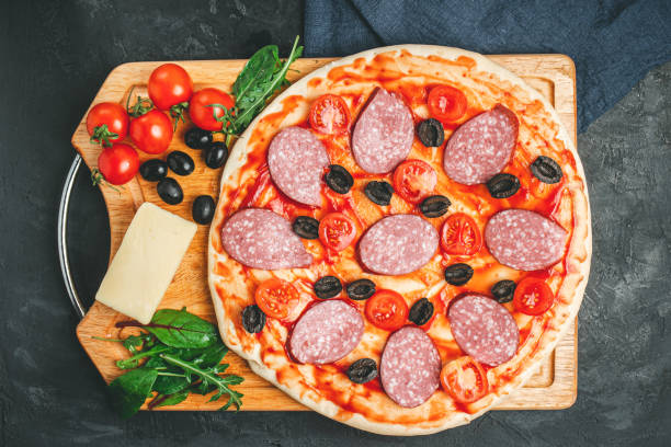 istock Process of making pizza round dough with black olives, cherry tomatoes, mozzarella cheese, sliced salami and green leaves spinach, rucola, top view 1206392300