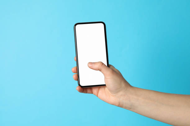 istock Female hand holding phone with empty screen on blue background 1206392605