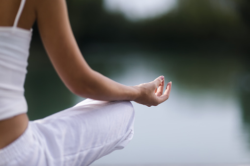 Close up of unrecognizable woman exercising in Lotus position outdoors. Focus is on hand.