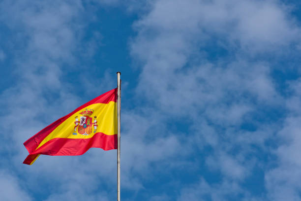 istock (Seville, Spain). Spanish Flag flies over a blue sky with white clouds 1206395706