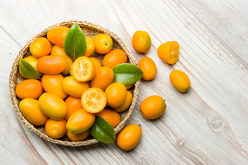 Kumquat fruits into basket on wooden table.