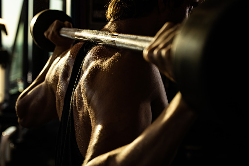 Close up of sweaty muscular build athlete doing back exercises with barbell in a gym.