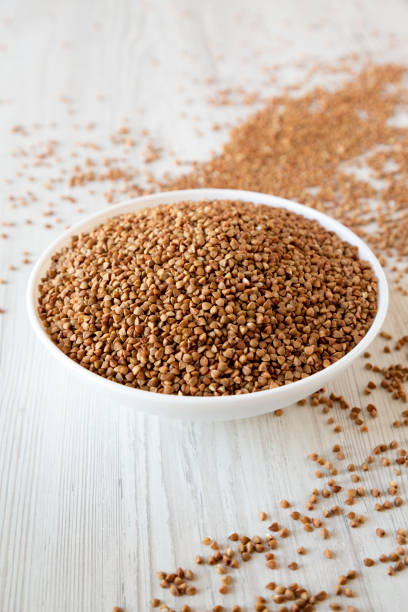 istock Uncooked Roasted Buckwheat in a white bowl on a white wooden background, low angle view. Close-up. 1206403122