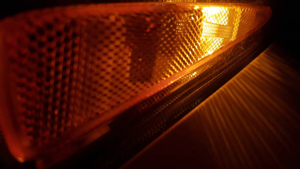 istock Closeup of patterned surface of orange color headlight on dark blurred background. Defocused light and striped rays in darkness. Abstract backdrop of glowing auto lantern. 1206403126
