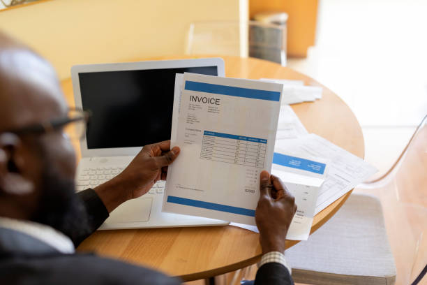 istock Shot of afro american young man in a home office using laptop and taking notes. Black guy sitting at table and working from home office. Worried Mature African is Looking at Financial Bills at Home Office 1206405949