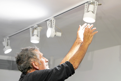 Elderly caucasian electric man changes ceiling LED lamps, spotlight. The concept of repair and maintenance.