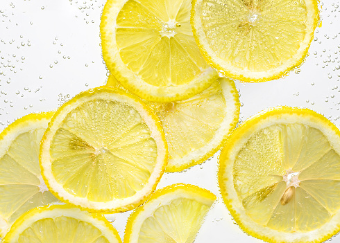 Slices of lemon in water with air bubbles on white background. Close-up
