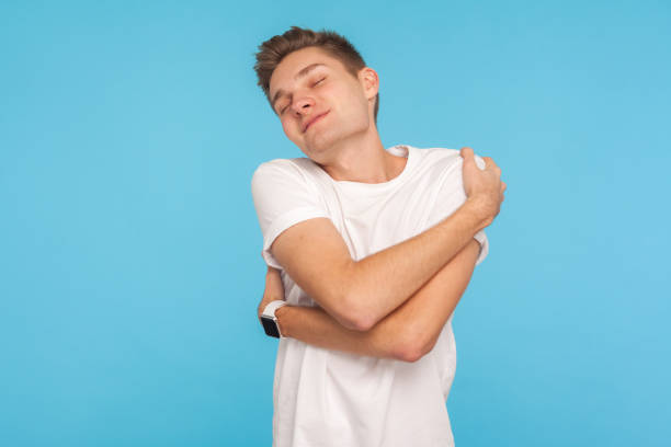 ego and high self-esteem. portrait of happy and selfish man in t-shirt embracing himself with expression of pleasure - urgency body care young adult people imagens e fotografias de stock