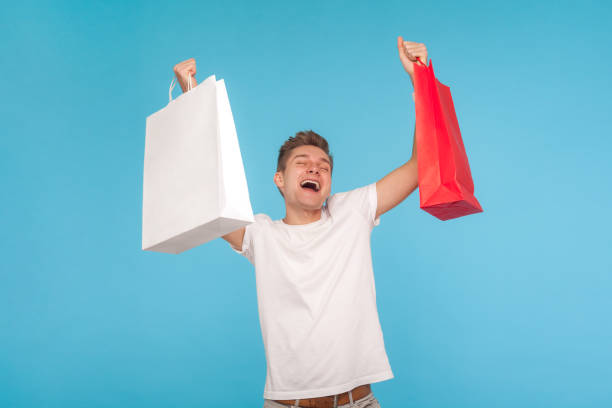 istock Overjoyed ecstatic man in t-shirt shouting enthusiastically and raising packages, holding shopping bags 1206411410