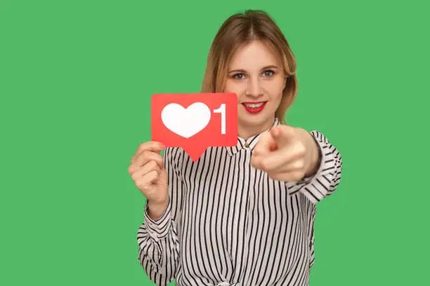 Photo of Hey you, put like to content! Pretty girl with red lips in glamour striped blouse holding social media heart icon