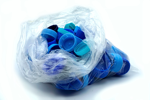 Blue plastic bottle caps sorted by colors in transparent single use plastic bags. PP an PET pollution. Recycling solutions for plastic waste.