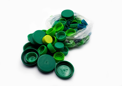 Green plastic bottle caps sorted by colors in transparent single use plastic bags. PP an PET pollution. Recycling solutions for plastic waste.