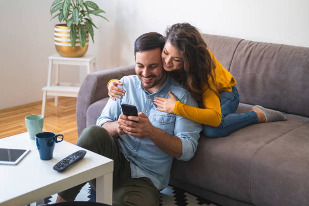 istock Couple embracing using mobile phone at home stock photo 1206423410