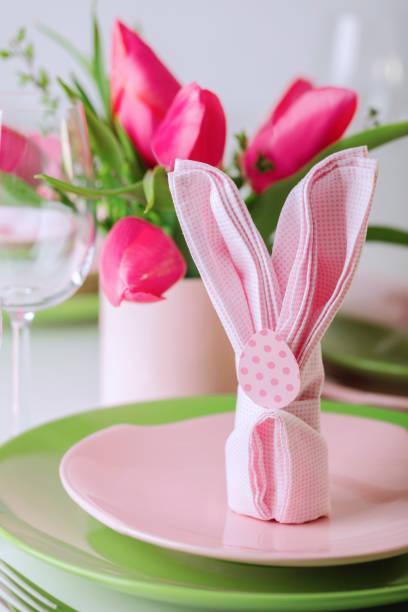Vintage-inspired Easter scene featuring a golden hanger suspending a wooden Easter bunny with dried flowers in its arms elegantly placed in front of a white porcelain milk jug filled with wildflowers. A small nest cradling an Easter egg adds a cozy festive touch. Color editing. Part of a series. Objects are decoration mass product.