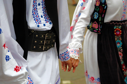 Professional dancers of the Timisul Folklore Ensemble hold hands in a traditional Romanian dance wearing traditional beautiful costumes.
