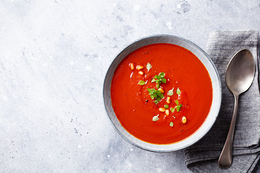 Tomato soup with fresh herbs and pine nuts in a bowl. Grey stone background. Copy space. Top view.