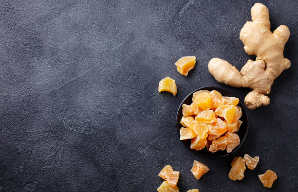Candied ginger in black bowl on dark stone background. Top view. Copy space.