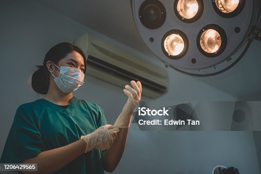 istock an asian chinese female surgeon getting ready and putting her surgical gloves on in the operating room illumined by surgical light 1206429565