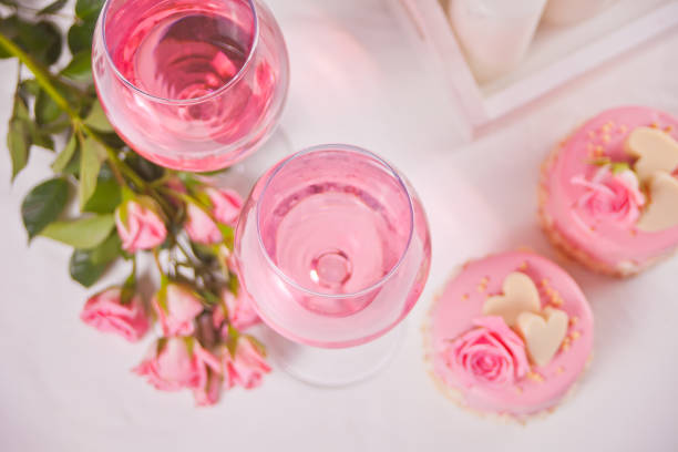 Two glasses with pink grape wine with flowers, gift box and mini cakes. Romantic dinner concept