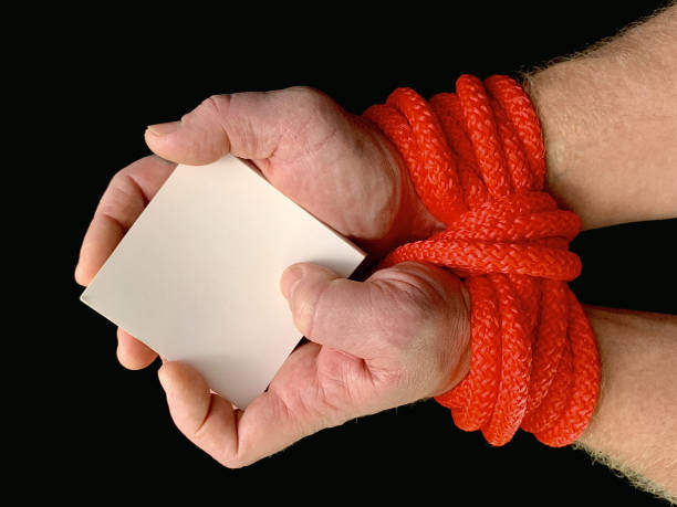 Hands tied with a rope, on a black background. Tied hands are holding a note with the inscription. Concept: loan, debt, help. Hands tied with a rope, on a black background. Tied hands are holding a note with the inscription. Concept: loan, debt, request for help terrorist financing stock pictures, royalty-free photos & images