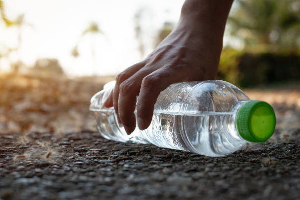 istock Close up Hand picking up clear plastic bottle water drink with a green cap on the road in the park at blurred background 1206439708