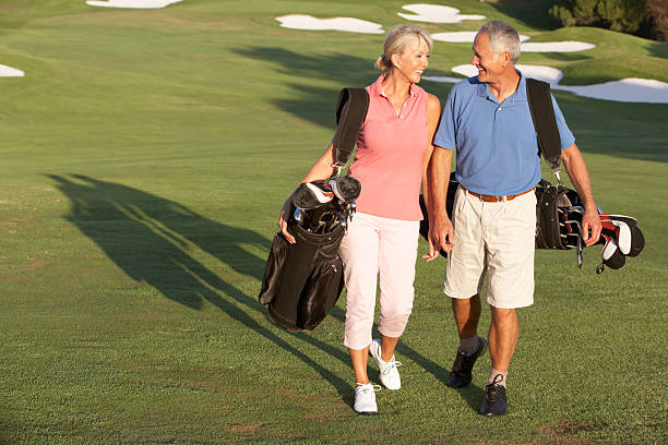 senior couple marchant sur le parcours de golf avec des sacs - playing golf photos et images de collection