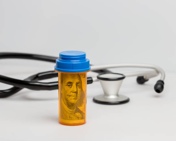 prescription drug, medicine pill bottle with 100 dollar bill inside with stethoscope on white background. concept of rising drug, health care, medical insurance cost - currency stethoscope medicare usa imagens e fotografias de stock
