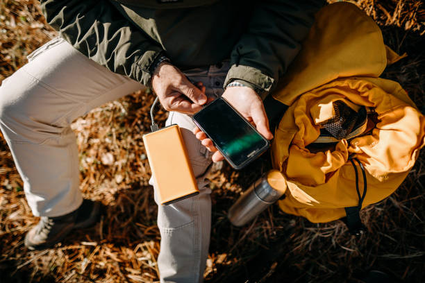 Man sitting in woods and charging mobile phone with power bank during beautiful day stock photo