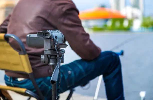 Photo of Close up of video camera filming young male blogger at city pond. depth of field blur